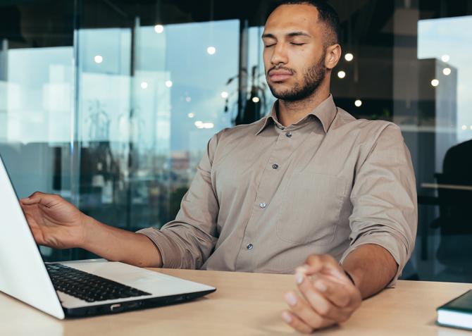 A person with their eye closed sitting at a desk.