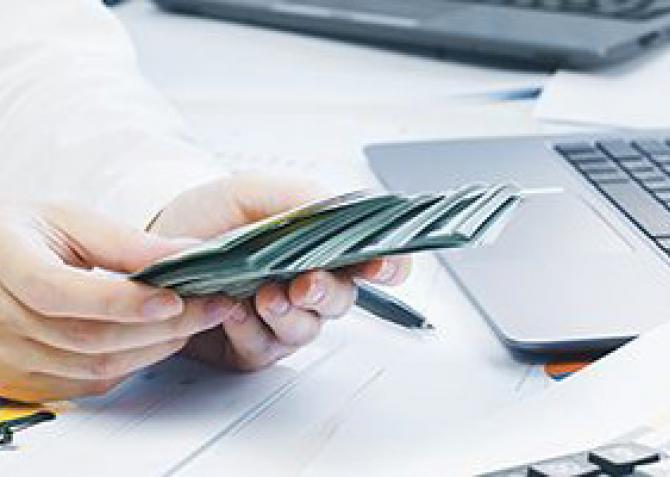 business man counting cash at desk with computer