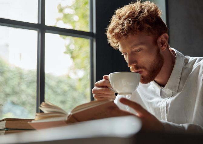 An entrepreneur drinks coffee while reading a book at a table.
